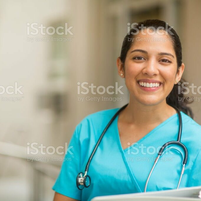 nurse2 Smiling female healthcare professional looks at the camera while in hospital hallway. She is standing with her arms crossed.